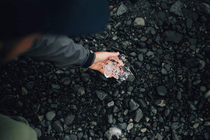 Hand holding ice on top of dark rocks