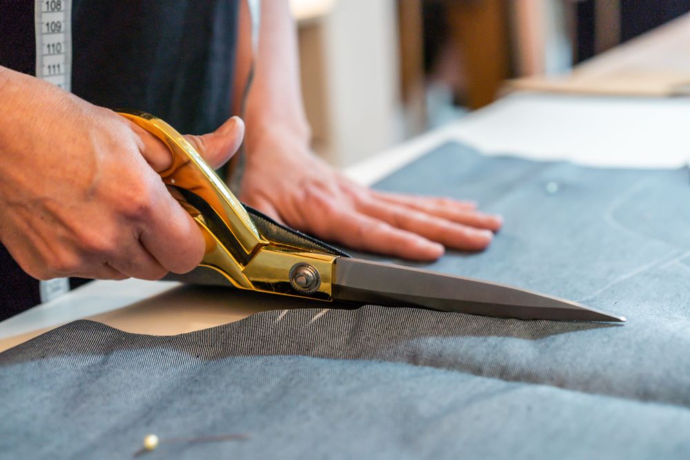 Close-up of fashion designer hands using scissors to cut textile at work table