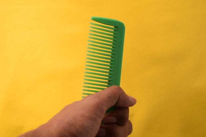 Hand with green hair comb with yellow background