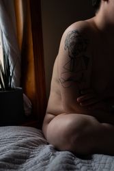 Cropped image of tattooed naked person sitting on bed bDM8E0