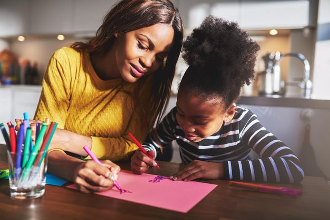 Black mother and daughter draw together in kitchen