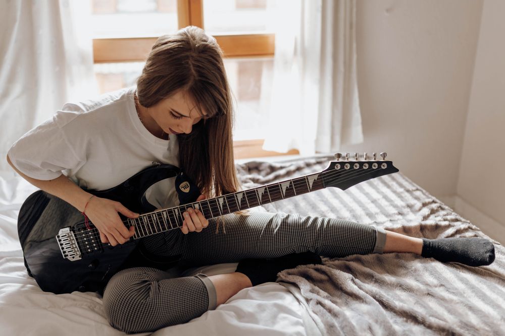 side view of Young brunette woman playing guitar on bed