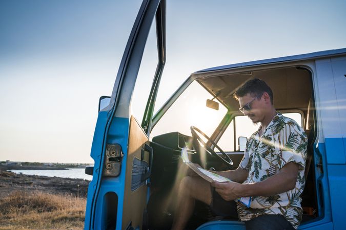 Adult man planing route for road trip while sitting in car on shore