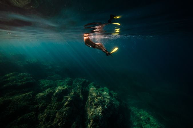 Unrecognizable man in flippers diving in blue ocean