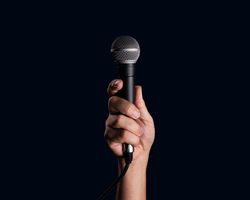 Hand holding a dynamic microphone on a dark background.