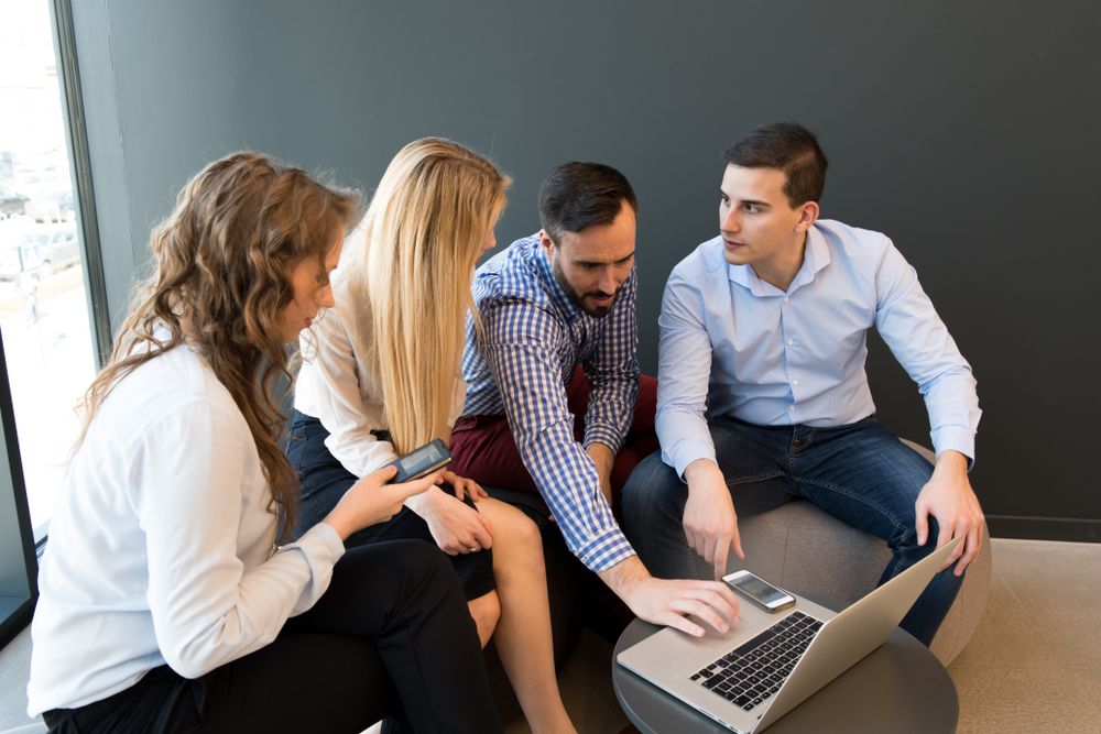 Stylish coworkers gathering around laptop in office