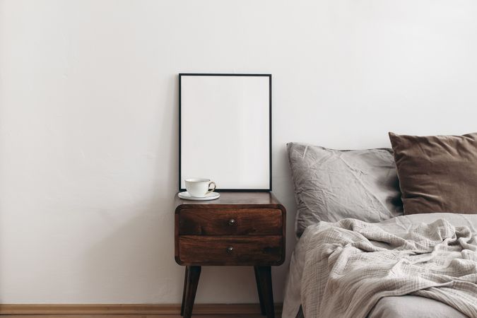 Vertical picture frame mockup next to cosy beige bed