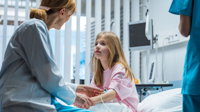 Recovering Little Girl Sits on a Hospital Bed and Talks with Friendly Woman Doctor