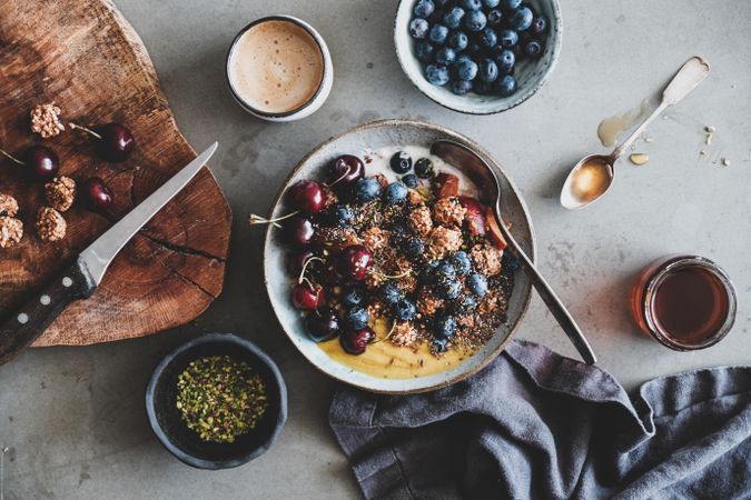 Oat granola yogurt bowl with cherries, blueberries, honey, nuts, coffee, wooden board, cloth napkin