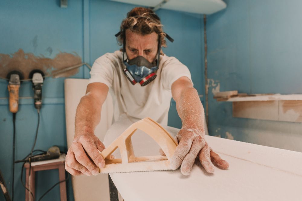 Man in respirator polishing surf board in workshop