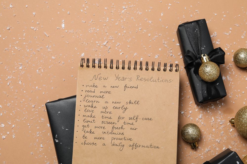 Paper with list, gift boxes and decorations on beige background, top view