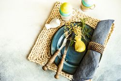 Top view of Easter table setting with navy plate with bird ornament and decorative eggs in cups