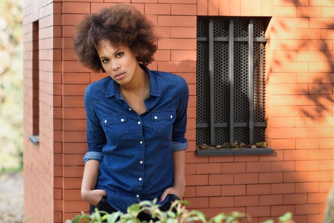 Female leaning on building with hands in her pocket looking at camera