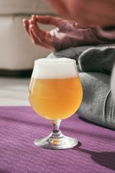 Glass of cold beer near woman on yoga mat