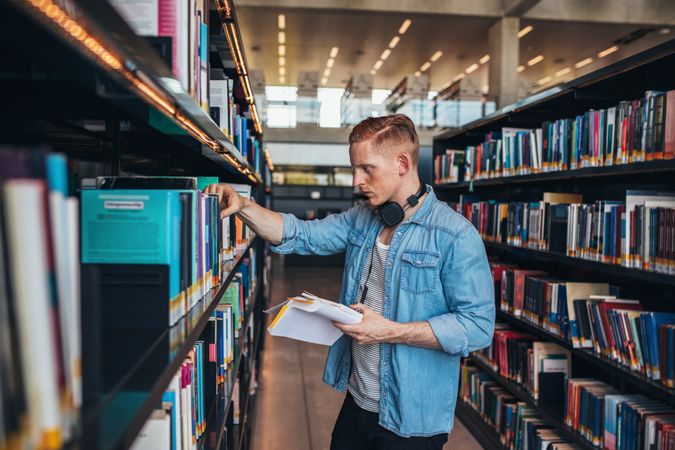 Young college student taking book from shelf in library