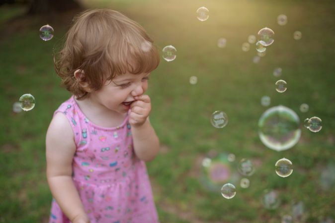 Joyful girl playing with colorful bubbles in grass