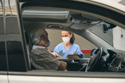 Crop physician talking to mature driver in car during drive thru