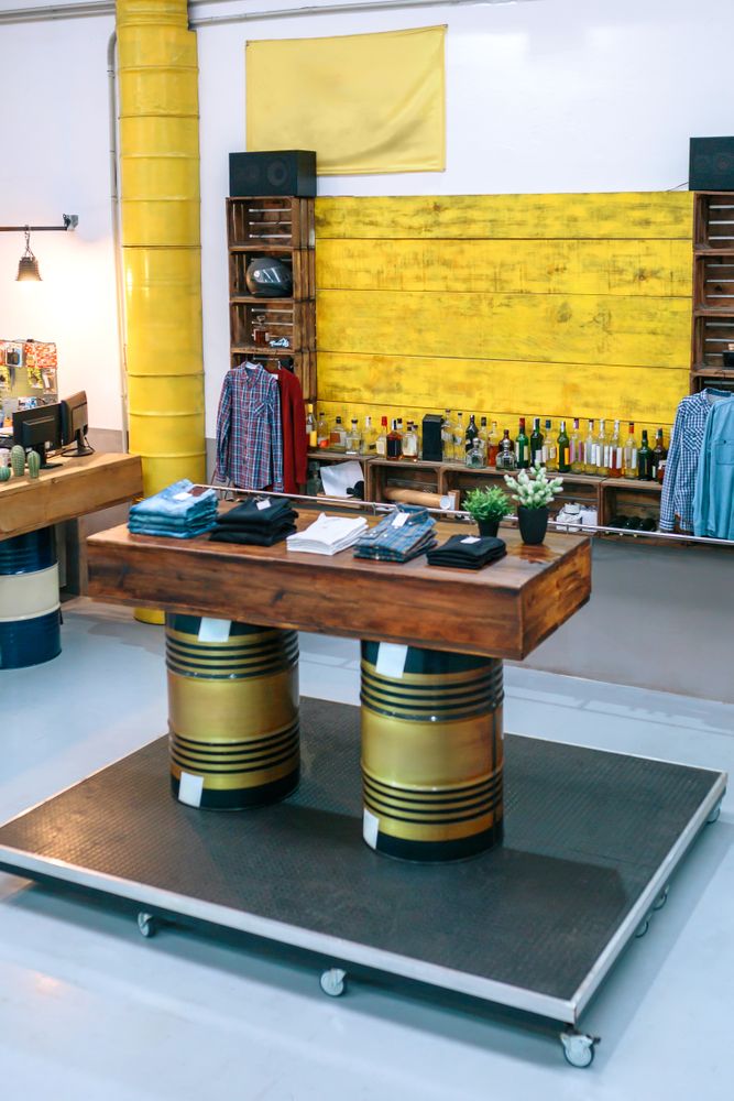 Interior of empty vintage apparel store with clothes over wooden counter supported by fuel barrels