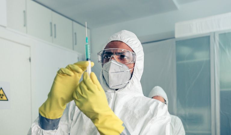 doctor in protective suit looking and preparing syringe with vaccine