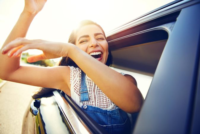 Happy woman with arms outstretched in celebration outside of car window