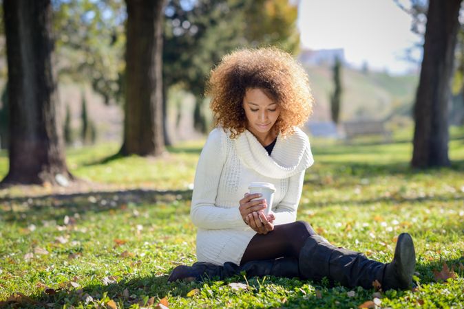 Sad woman looking down at warm beverage while sitting alone in park