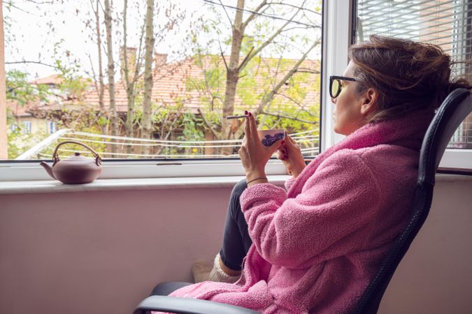 Woman in cosy clothes holding cup of tea and spliff