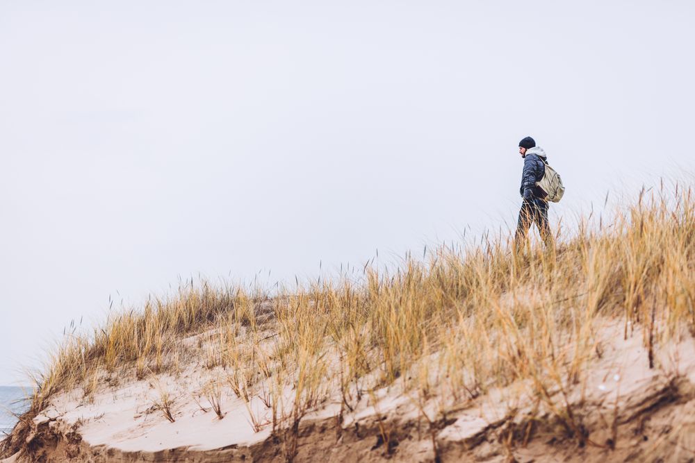 Man walking between sand field with dry grass