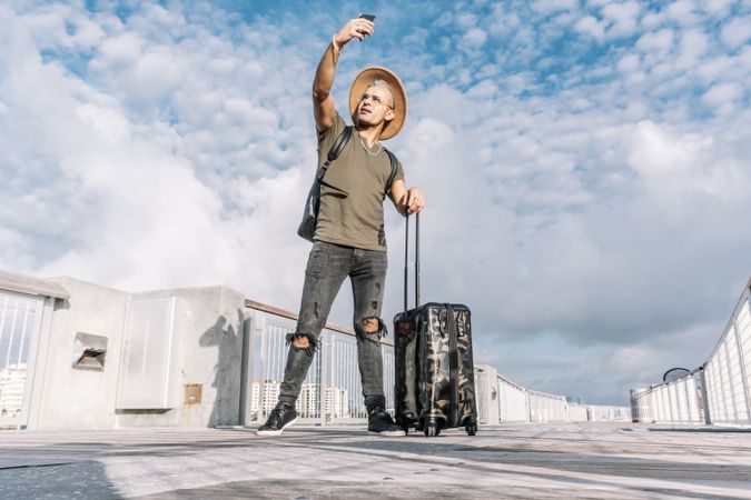 Full length portrait of a hipster man taking a selfie with a suitcase