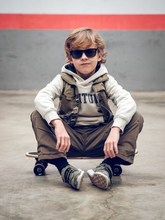 Boy in trendy outfit sitting on skateboard