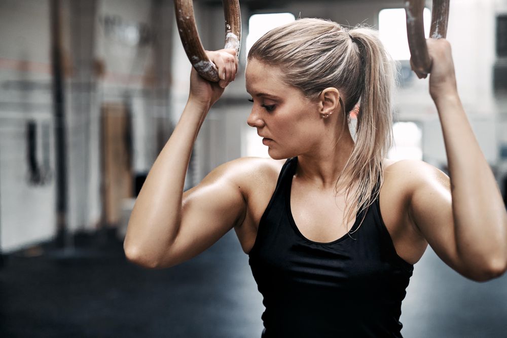 Healthy woman holding onto gymnastic rings and looking away