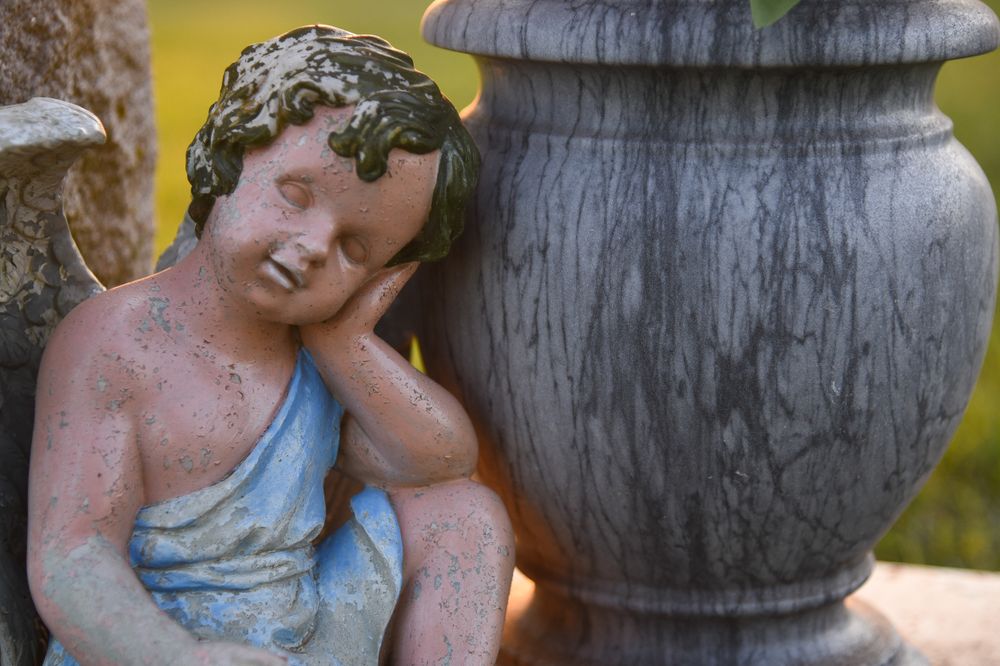 a sleeping angel by a flower pot in a cemetery