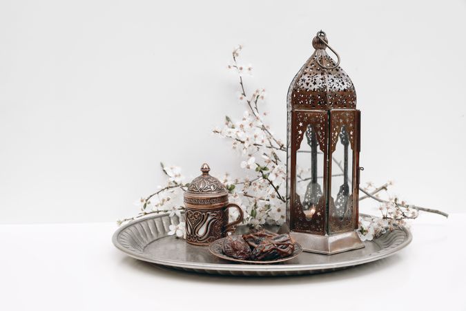 Date fruit, flowers cup of tea and glowing Moroccan lantern on silver plate