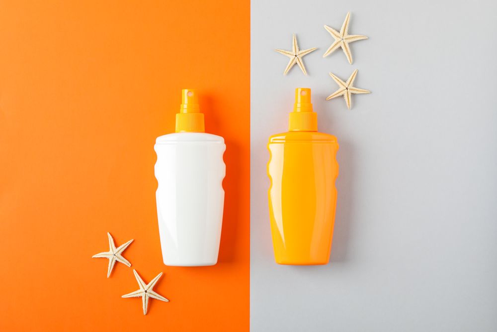 Flat lay composition with sunscreen sprays and starfishes on two tone background, space for text. Summer vacation backdrop