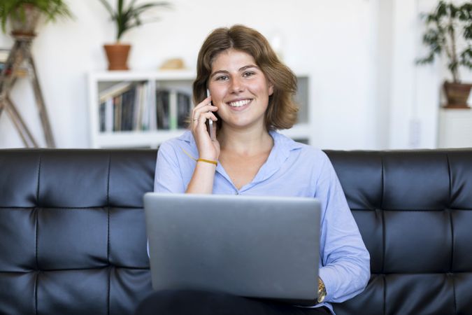 Female entrepreneur sitting on couch at home using a laptop and speaking on phone