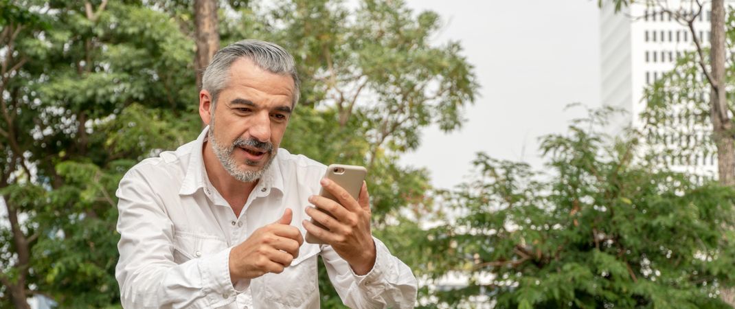 Mature grey haired man texting in park