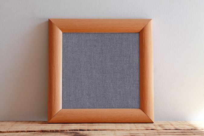 Plain square wooden picture frame with grey interior leaning against wall mockup