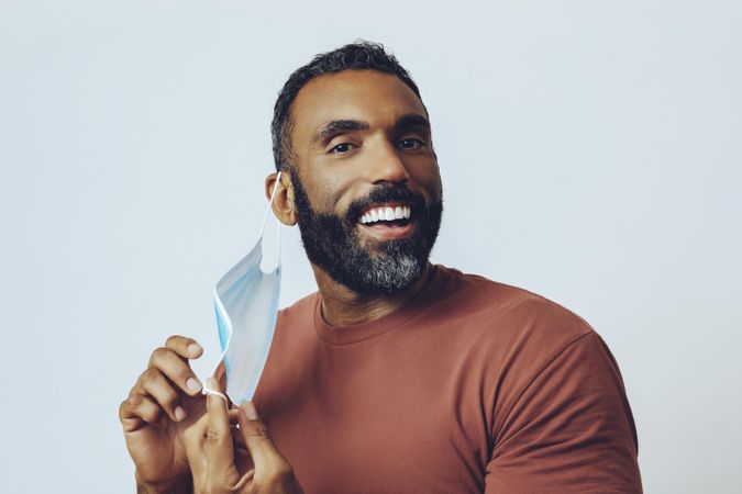 Happy male adjusting his medical face mask looking at camera in studio shoot