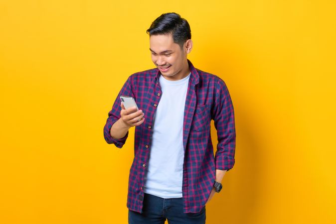 Smiling Asian man in plaid shirt  looking down at smartphone