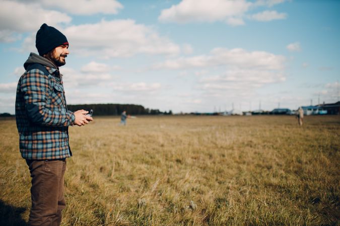 Side view of a man in plaid shirt holding a drone controller standing on grass field