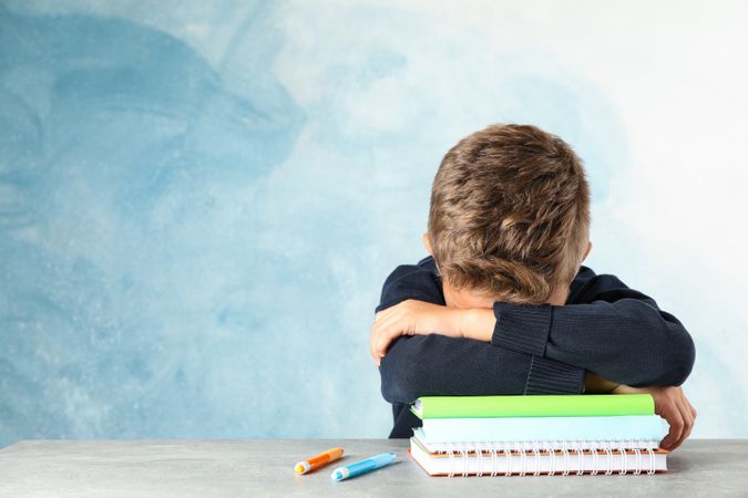 Boy sleeps on notebooks heap against color background, space for text
