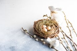 Speckled eggs in nest on table with pussy willow branches and rabbit figurines with copy space