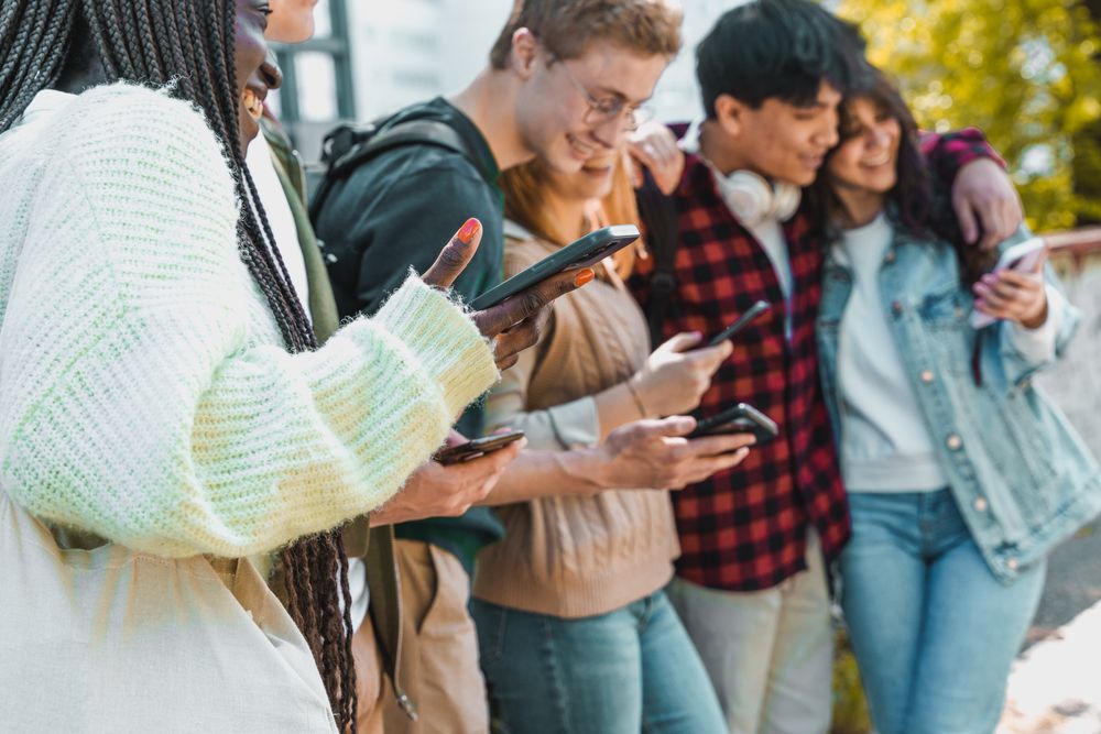 Multi-ethnic group of students hanging out on campus using their phones