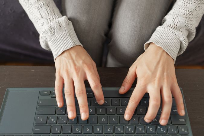 A woman types on her laptop while sitting on the sofa at home.