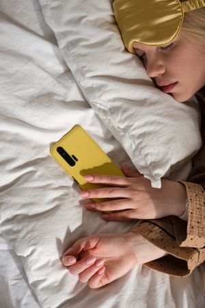 Woman asleep with phone, wearing eye mask