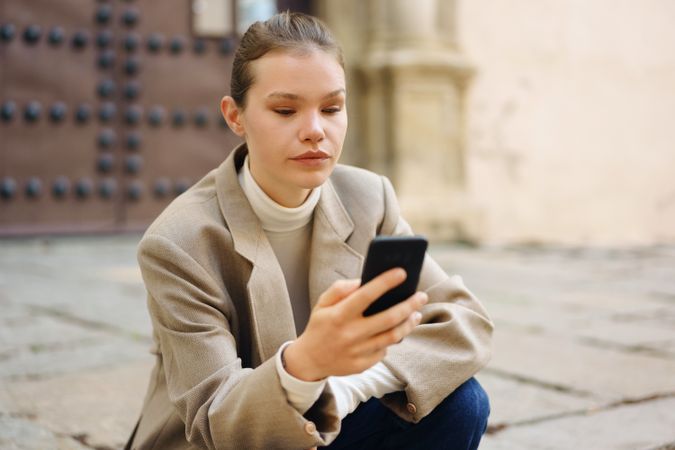 A Young Woman is Engaged with Her Smartphone While Sitting Outdoors in a Public Space