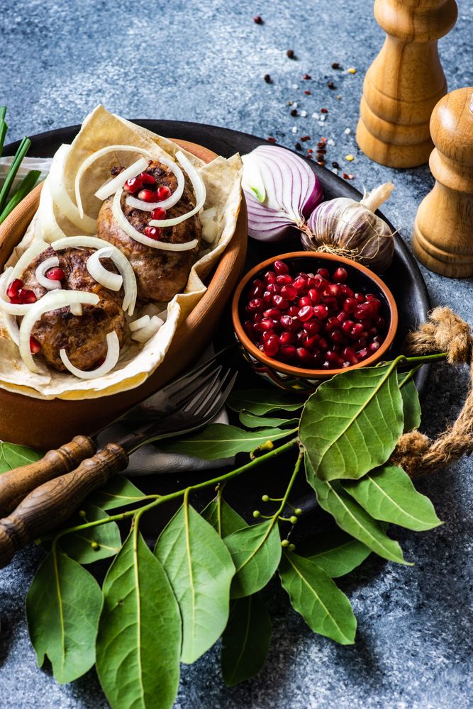 Georgian dish of abkhazura meat cutlets on plate with pomegranate seeds and bay leaves
