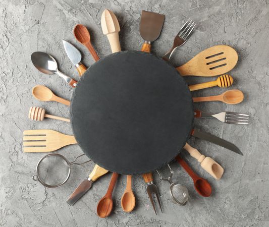 Composition with different kitchen cutlery and round cutting board on gray background