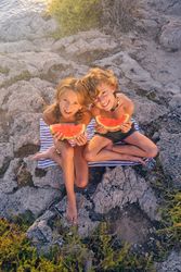 Glad preteen kids with watermelon slices sitting on rocky coast