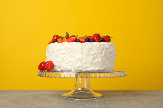 Berry cream cake against yellow background. Delicious dessert