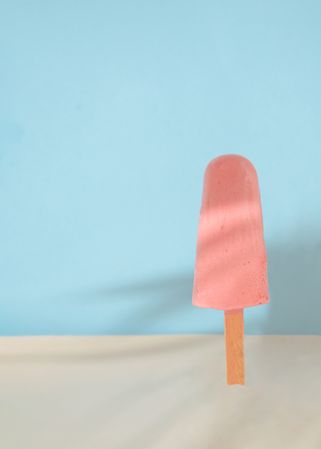 Pink ice pop on blue background with sand